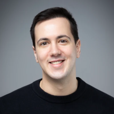 Professional headshot of Andrei Racasan, smiling and dressed in a collared shirt with a dark sweater